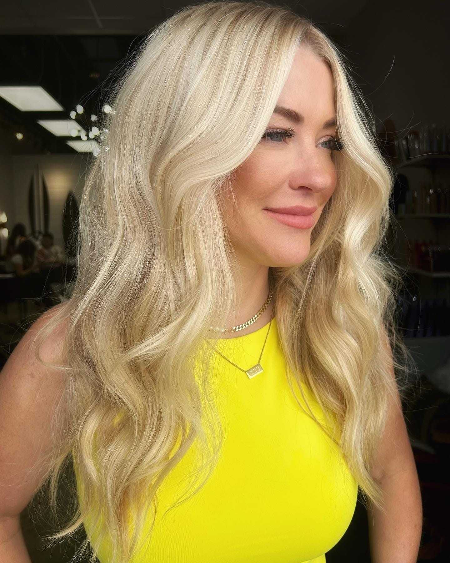 Blonde woman with long wavy hair wearing a bright yellow top, smiling.