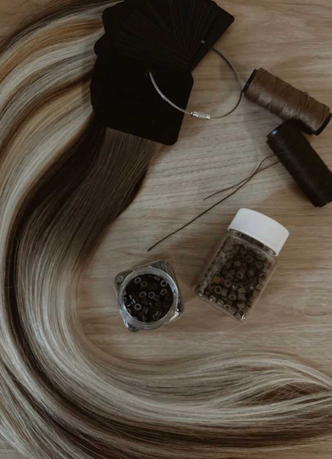Hair extensions and tools on a wooden surface, featuring color samples and beads.
