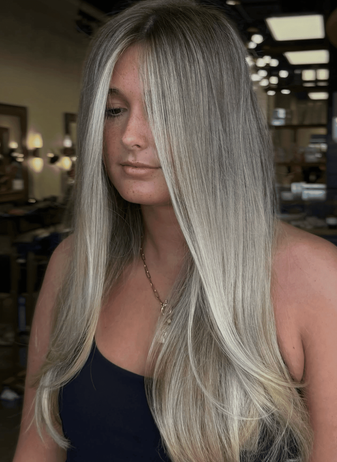 Blonde woman with long straight hair in a salon, wearing a black top.