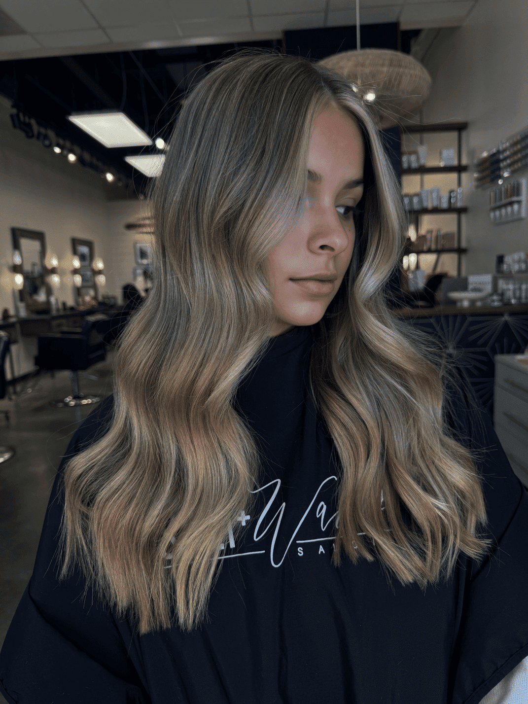 Woman showcasing long wavy blonde hair in a modern salon setting.