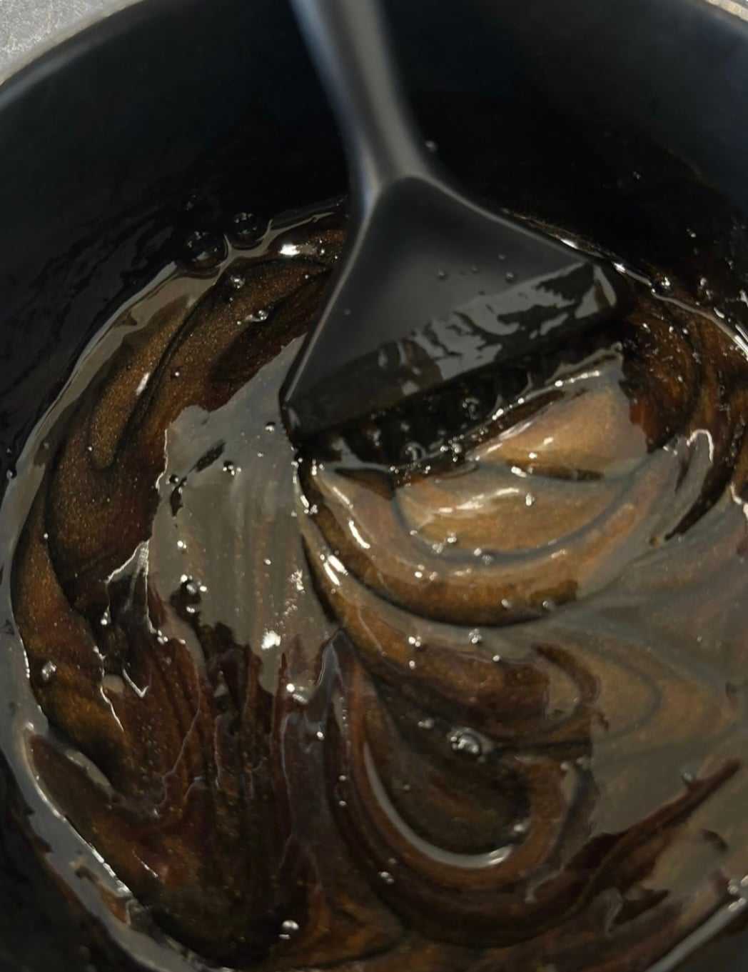 Black brush stirring glossy brown caramel in a pan.