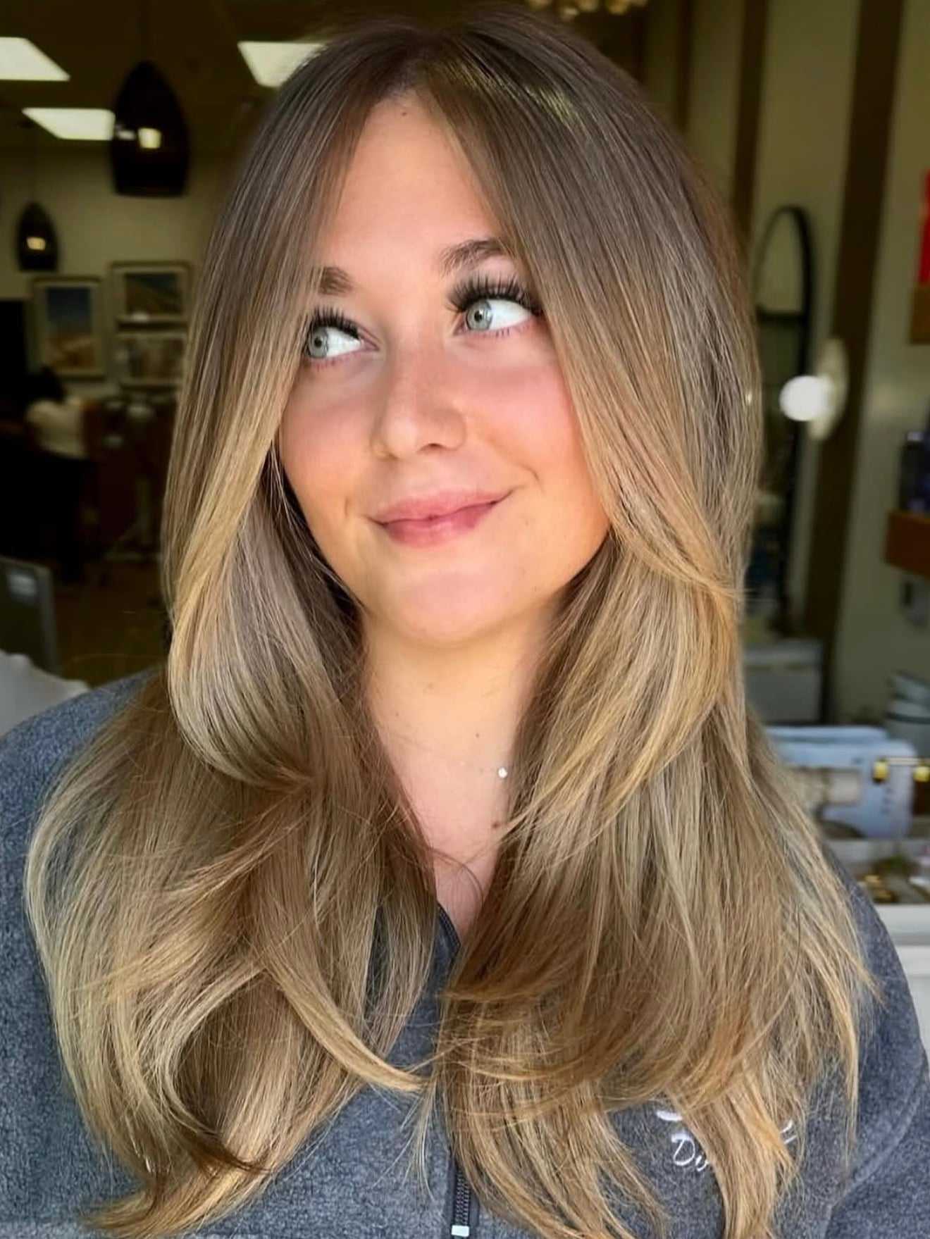 Young woman with long, layered brown hair smiling in a salon setting.