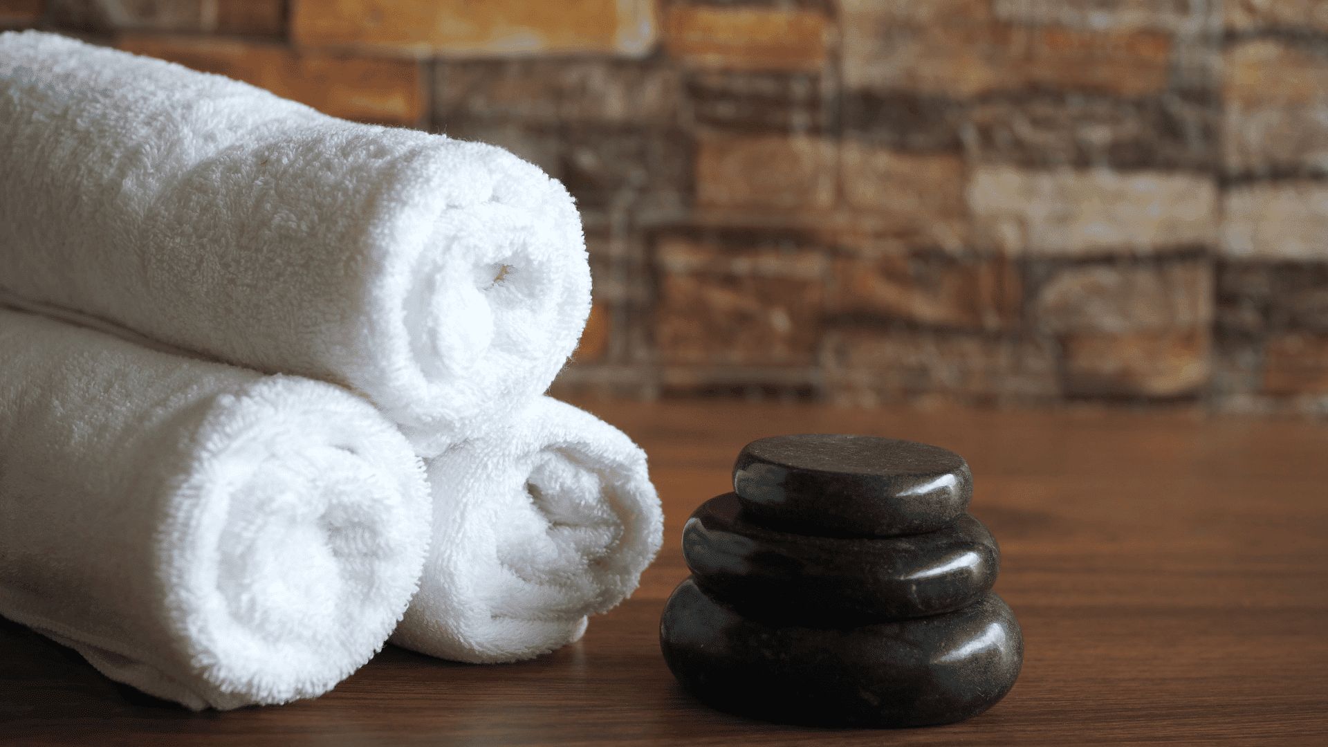 Rolled white towels and stacked stones on a wooden table.
