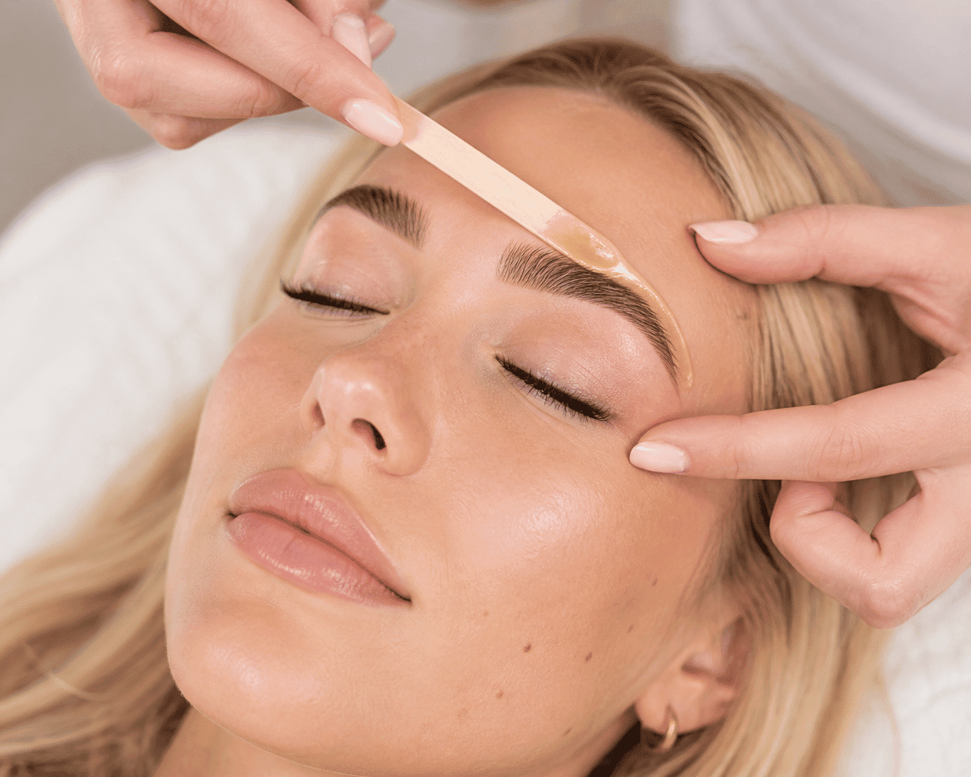 Eyebrow waxing treatment on a woman with closed eyes, showcasing beauty care.