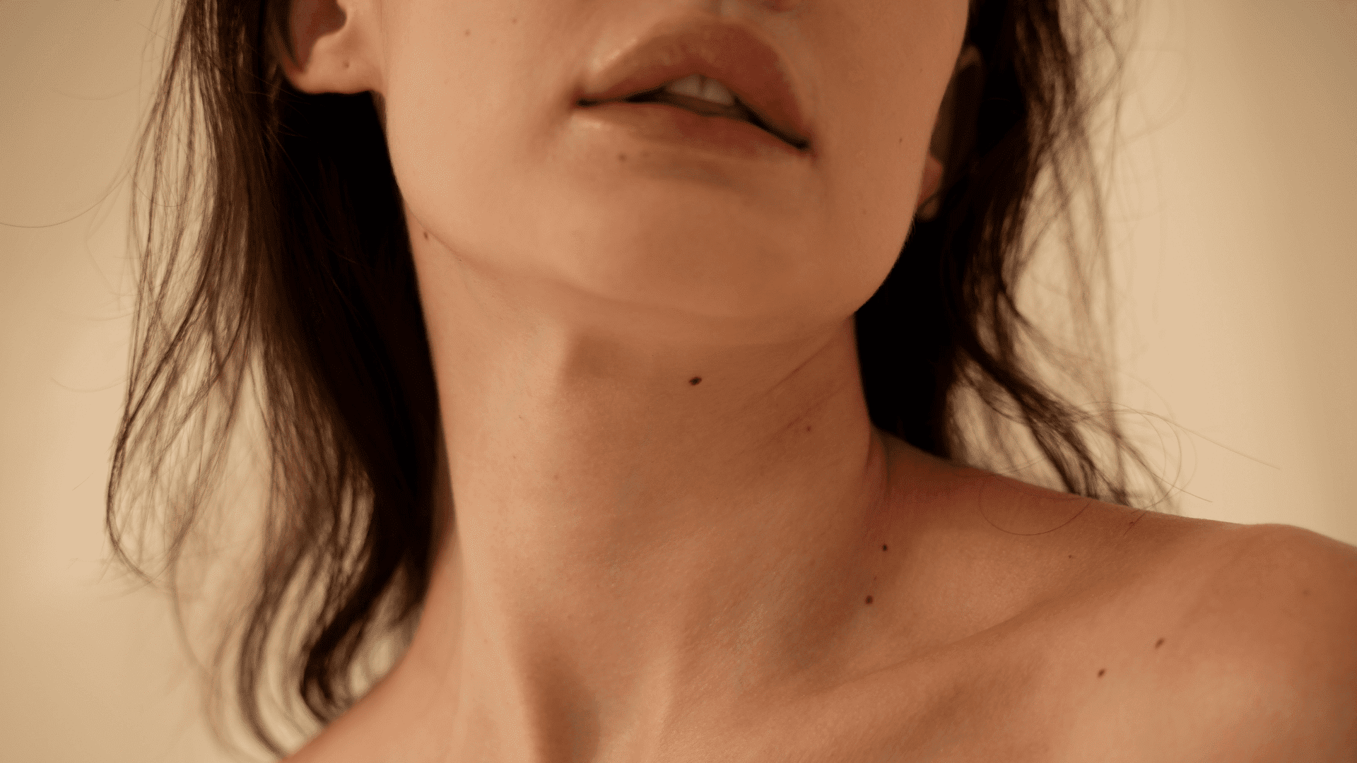 Close-up of a woman's neck and lips, soft lighting, with delicate freckles visible.