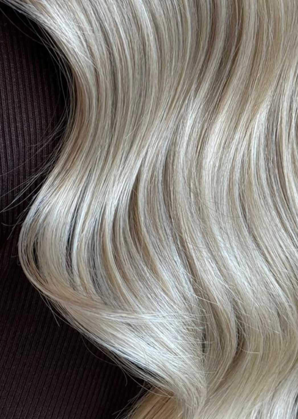 Close-up of long, wavy, blonde hair against a dark textured fabric background.