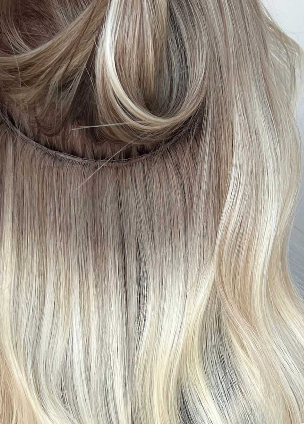 Close-up of wavy blonde hair with visible extension attachment.