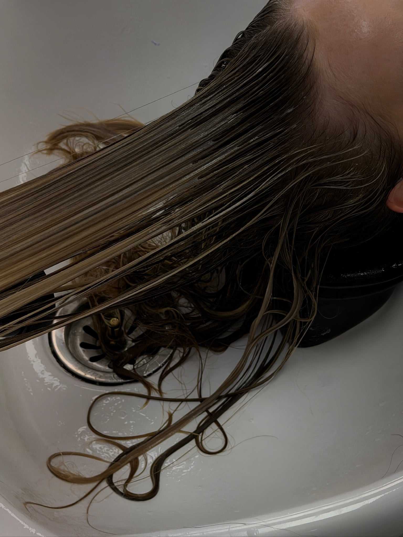 Person washing hair in a white sink, water running through long wet strands.