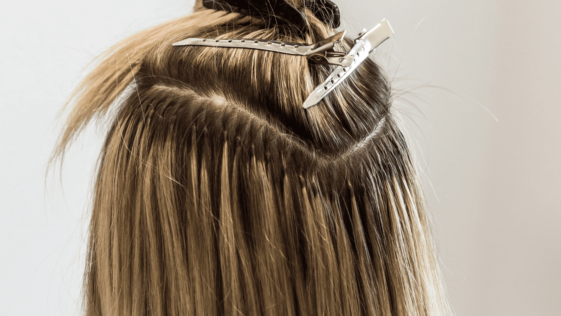 Hair extensions being applied with metal clips in a salon setting.
