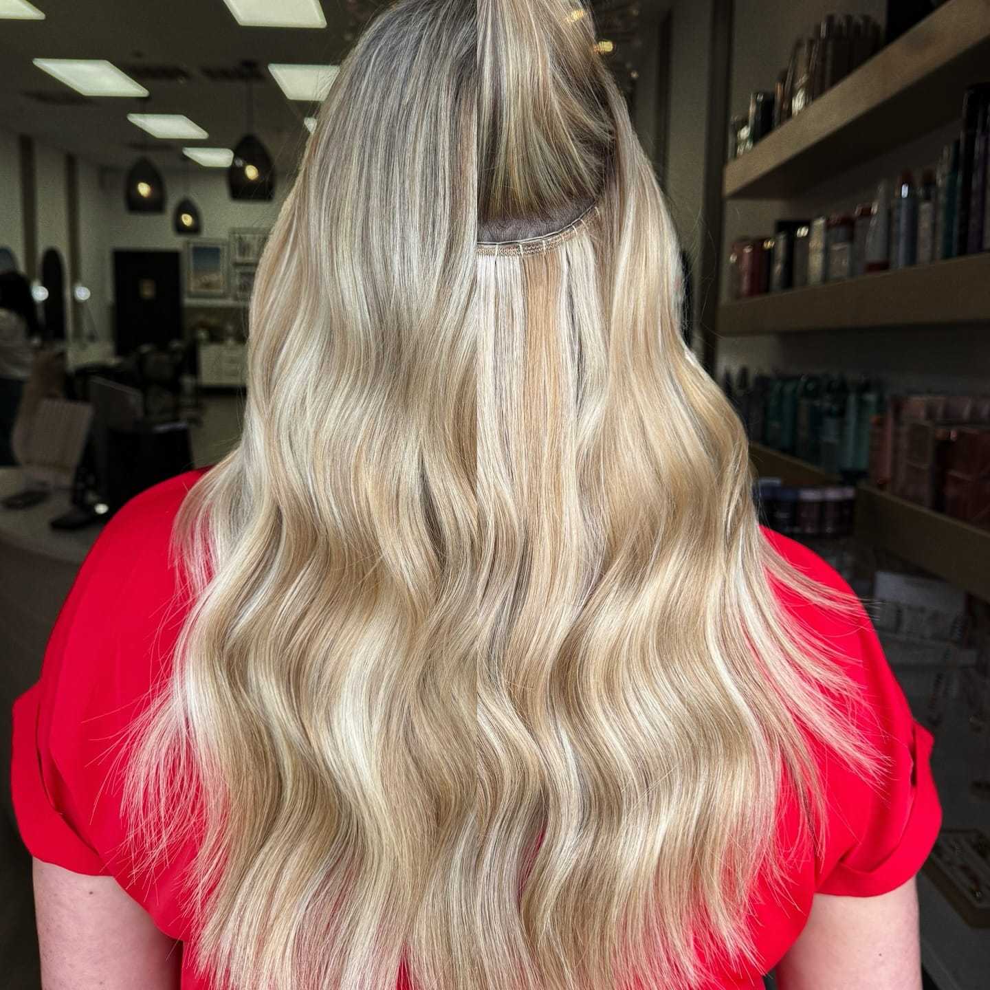 Blonde hair with extensions styled in waves, seen from behind in a salon.